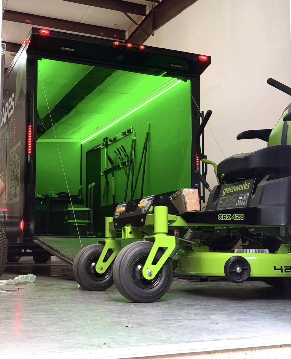 Greenworks battery-electric riding mower beside the open QuietScapes trailer